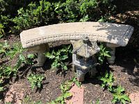 Curved concrete garden bench and concrete pagoda lantern shown outdoors surrounded by vegetation.