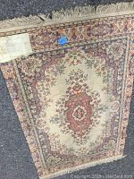 Photo of the front of the wool area rug showing detailed traditional floral medallion design with red, cream, and blue colors and fringed edges.