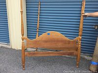 Wooden bed footboard with turned posts and a slightly arched panel design, showing part of the side rail attached.