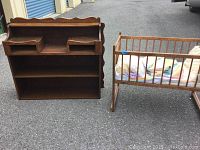 Photo showing the wall shelf with three large shelves and two small pigeonholes, and the adjacent wooden doll cradle with bedding included.