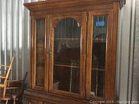 Front view of the Broyhill illuminated cabinet showing wood finish, glass doors with brass handle, and interior shelves.
