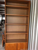 Full view of tall wood shelf unit with five shelves and bottom cabinet with closed doors.