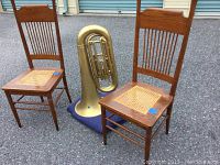 Front view of two cane chairs with woven cane seats and a large replica brass tuba standing between them.