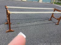 Full view of the wooden quilter stand showing the two horizontal bars and wooden end supports on an asphalt surface.