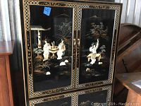 Front view of Asian black lacquered media cabinet showcasing detailed artistic inlays of traditional Asian figures and landscape on door panels.