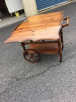 View of wooden beverage cart with scalloped tabletop, drop sides, wooden wheels, and handle.