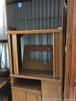 Media cabinet showing front glass doors with wooden frame, open shelf below, and bottom enclosed cabinet area.