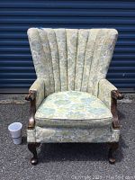 Front view of vintage wing back chair against blue storage background, showing seat, back, armrests, and wood legs with cup placed to show scale.
