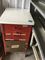Front view of vintage tool box on wheels showing white top and red metal drawers with labels