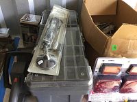 Photo showing a clear-lid gray plastic storage box topped with a packaged chrome light fixture and a cardboard box nearby with some parts.