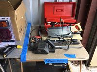 Photo of table with various hand and power tools including a red toolbox, hand saw, and electric planer.
