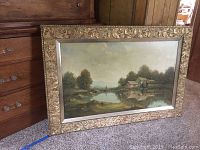 Frontal view of the framed painting on carpet floor, showing entire artwork and ornate frame.