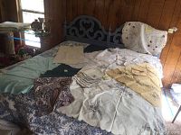Various vintage table linens including tablecloths and napkins spread across a bed showing pattern variety and colors.