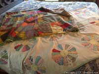 Two handmade quilts displayed folded and spread; patchwork quilt with multiple fabric patterns and circular pattern quilt with multi-colored circular segments on cream background.