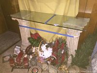 Wide angle photo of the console table showing the entire glass top and both supporting columns with some decorative holiday items below.