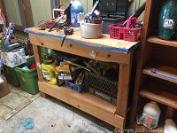 Wood work bench with items on top and lower shelf, including toolboxes and storage baskets