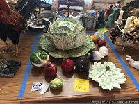 Overview of entire set showing cabbage soup tureen with lid on matching platter, two plates, and assorted faux vegetable ceramic pieces including pomegranates, cabbage, eggplant, onions, and more arranged on a table.