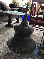View of the assembled brass chiminea showing its rounded body and perforated decorative details with top finial.