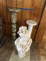 Overview of the three items: Italian marble pedestal, ceramic pedestal, and female bust statue on carpet in front of wood panel wall.