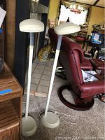 Two matching white daylight floor lamps standing side by side. Each has a round base, a flexible grey neck, and a rounded rectangular lamp head. Lamps are approximately 60 inches tall.