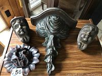 Overview of four carved wood items on a wooden surface: two carved faces, a sconce, and a flower-shaped piece.