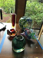Five Italian Murano glass decorative pieces including vases, bowls and tea light holders arranged on a table by a window.