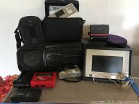 Photo showing the full lot including Sanyo boom box, cameras, digital photo frame, photo printer, and cases