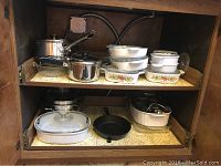 Full view of upper and lower shelves with cookware assortment including Pyrex dishes, CorningWare casseroles, WearEver stainless pots, cast iron skillet, and egg poacher.