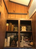 Wide view of wooden cabinet containing pillar candles, candle holders, wall art, and other decorative accessories.