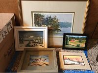 Photo showing all five framed paintings grouped together on carpet against wood panel wall, various sizes and frames visible