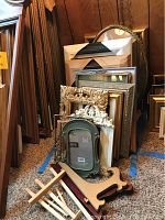 Various frames and wooden easel and plate racks arranged together on carpeted floor against wooden panel wall