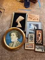 Overview of 7 art pieces including carved wooden bust, round gold-framed portrait, and 5 smaller framed works on carpeted floor