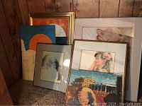 Group photo showing six original MaryAnn Young artworks, some framed, others unframed, leaning against a wood-paneled wall.