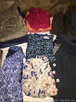 Top view of folded women's clothing items showing various tops, sweaters, jackets, skirts, and bottoms in neutral and bright colors.
