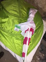 Photo showing the green nylon leaf canopy laid flat with the pink and white striped beach umbrella folded and wrapped in plastic placed on top