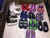 Photo showing an assortment of toddler footwear including character slippers, sneakers, sandals, slides, and two pairs of skates laid out on a white fabric.