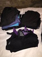 Photo shows stacks of long sleeve tees and sports bras in primarily black, purple, and blue colors, from workout wear selection