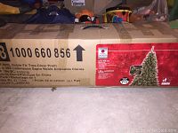 Boxed 6.5 ft pre-lit Noble Fir Christmas tree with clear lights from Home Heritage brand. Box label visible showing product details and weight of 10.1 kg.
