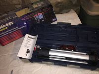 Laser level kit box and carrying case open with tripod and manual inside, displayed on a table.