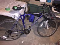 Side view of complete blue Mongoose Hill Topper mountain bike with helmet hanging on handlebar and bag strapped on frame, showing overall condition, tires, and frame details.