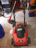 Front view of the Black & Decker electric lawn mower with trimmer resting on it.