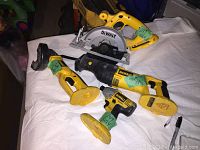 Four yellow and black DeWalt cordless power tools arranged on a white sheet: circular saw, reciprocating saw, cut-off tool, and impact driver