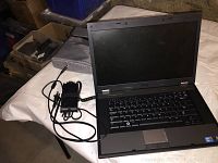 Dell Latitude E5510 laptop open, keyboard and screen visible, power cord plugged in.