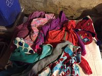 Toddler outerwear items including jackets, raincoats, hoodies, and accessory set laid out on a soft surface with a stone wall background.