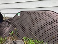 Disassembled metal chairs and table parts stacked outdoors on gravel and near a building exterior wall. Visible rust and weather wear on metal surfaces.
