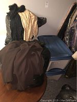 Two large black plastic bags and one blue and white plastic tote filled with women's clothing, showing outerwear and coats on top.