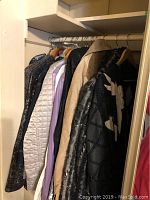 Side view of several jackets on hangers showing different colors and textures including black, beige, purple, and other dark colors