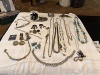 Multiple vintage costume jewelry pieces including necklaces and earrings laid out on white cloth, showing various designs, styles, and material finishes.