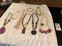 Full view of the necklace and ring lot arranged on a white cloth, showing a variety of necklace styles and one large pendant ring.