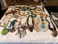 Full spread of assorted vintage costume jewelry, necklaces, bracelets, and brooches arranged on a white cloth.
